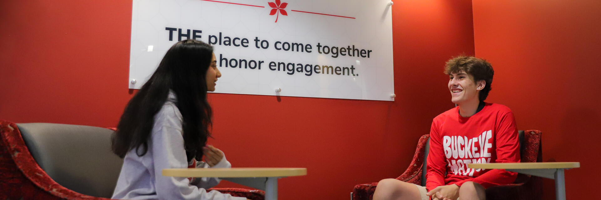 Two students sit in chairs and talk in front of Buckeye Commons sign.