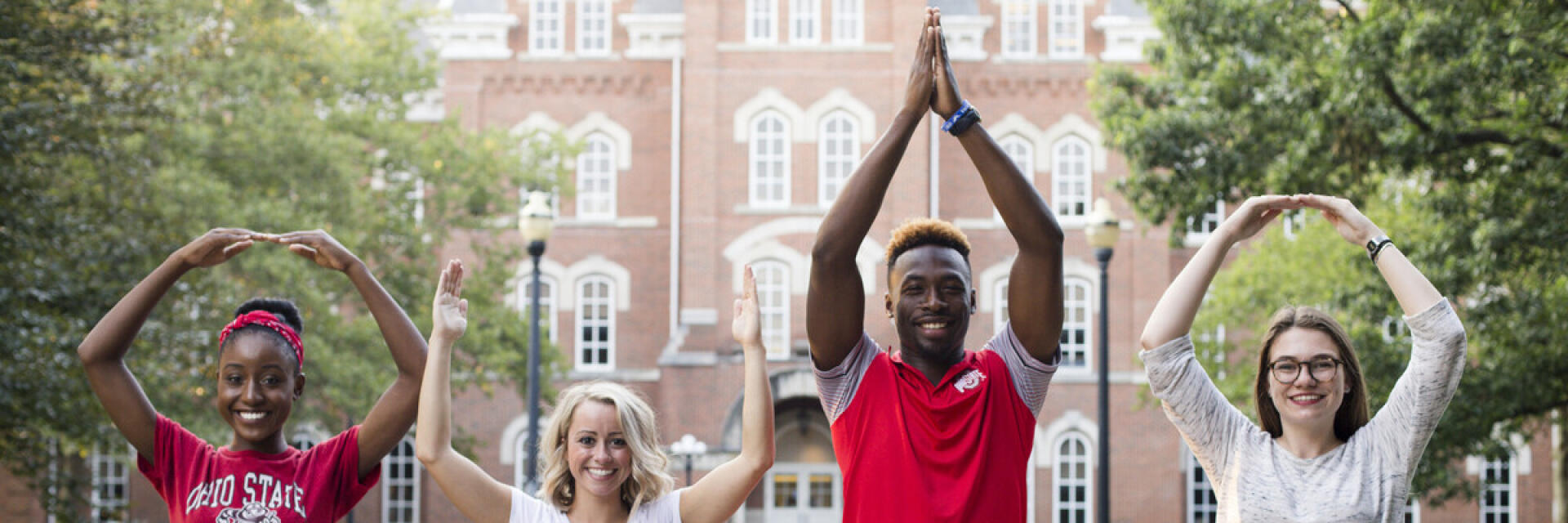 Four students doing the iconic O-H-I-O in front of University Hall