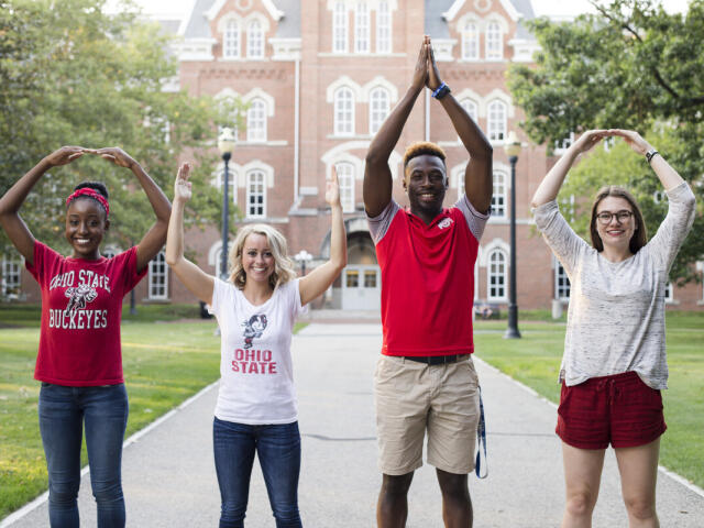 Four students doing the iconic O-H-I-O in front of University Hall